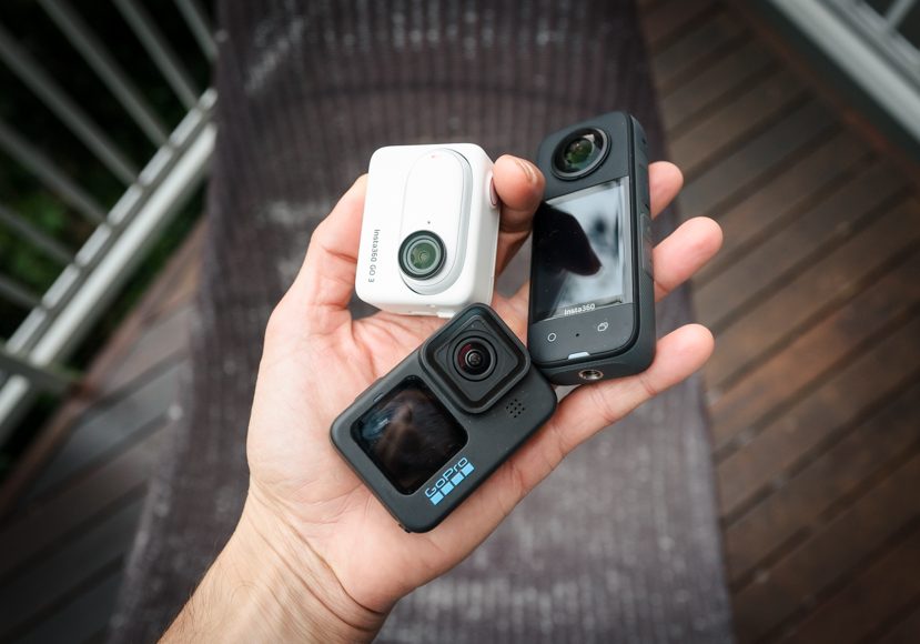 A person holding two action cameras on a deck. A person holding two action cameras on a deck.