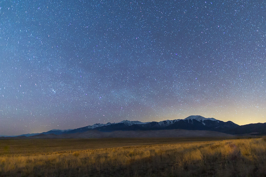 Starry night sky over a vast, open landscape with distant mountains on the horizon.
