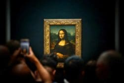 A framed painting of the Mona Lisa displayed in a dark room with a crowd of people taking photos in front of it.