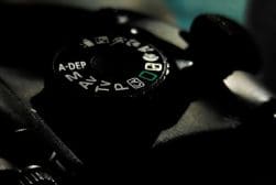 A close-up of a camera mode dial displaying various settings such as A-DEP, M, Av, Tv, P, and others, illuminated under low light.
