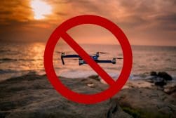 A drone is shown with a prohibition symbol in front of a sunset over the ocean, indicating a no-fly zone.