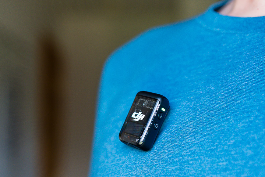 A small, rectangular electronic device with the DJI logo clipped onto a person's blue shirt.