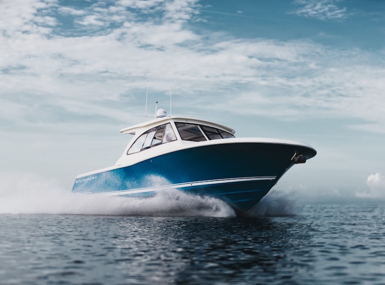 A blue motorboat speeds across the water under a partly cloudy sky.