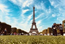 People relaxing on a grassy field near the Eiffel Tower under a blue sky with scattered clouds.