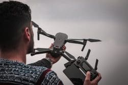 A person holding a drone in one hand and a remote controller in the other, preparing for takeoff against a cloudy sky.