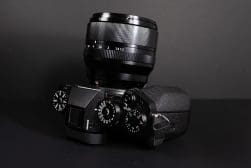 A black mirrorless camera with a large lens and several control dials is placed against a dark background.