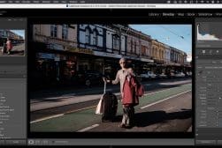 A person with a suitcase and a jacket stands on a street with various shops in the background. The image is displayed within the Adobe Lightroom Classic interface.