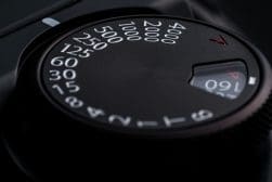 Close-up of a camera dial displaying various shutter speed settings, ranging from 1 second to 1/4000 of a second, with numbers in white against a black background. A small indicator points to 1/60.