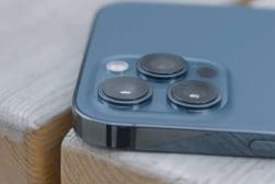 Close-up of a blue iPhone with triple camera system resting on a wooden surface.