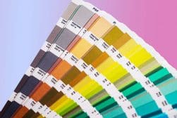 A color fan deck showing various Pantone swatches arranged in a gradient from gray to green to blue, against a pink and purple background.