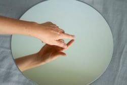 A person's hand reaching into a mirror.