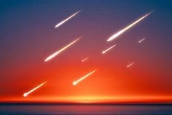 Multiple bright meteor trails streak across a colorful sunset sky over a calm ocean.