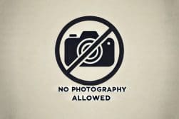 A "No Photography Allowed" sign with a crossed-out camera symbol on a beige background.