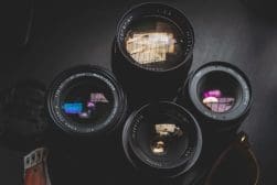 Assorted camera lenses on a dark surface, reflecting ambient light.