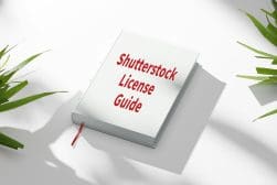 A book titled "Shutterstock License Guide" lies on a white surface, surrounded by green leaves, with a red ribbon bookmark hanging from its pages.