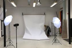 A person adjusts a large white backdrop in a photography studio equipped with lighting equipment and softboxes.