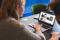 Two people looking at photos on a laptop screen while sitting at a table. One person is pointing at the screen.